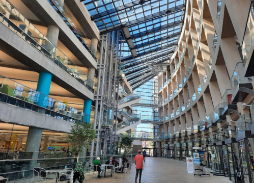 Modern library interior with glass ceiling, open spaces, and people engaging in various activities.