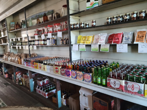A rustic store shelf filled with various bottles, jars, and colorful soda cans, showcasing a variety of products.