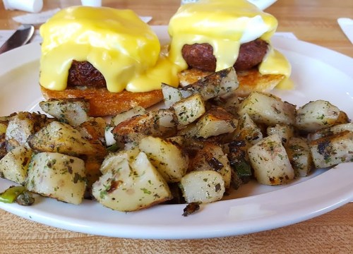 A plate of eggs Benedict with two poached eggs and cheese on toasted English muffins, served with seasoned roasted potatoes.