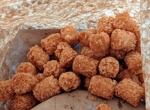 A close-up of golden-brown, crispy tater tots in a paper bag.