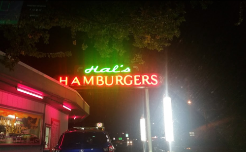 Neon sign for Hal's Hamburgers illuminated at night, with a retro diner aesthetic and surrounding trees.