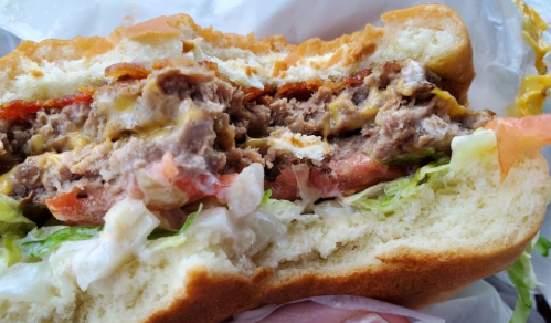 Close-up of a half-eaten burger with layers of meat, cheese, lettuce, tomato, and mayonnaise in a soft bun.