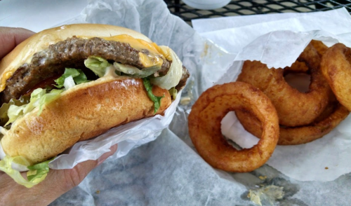 A hand holding a cheeseburger with lettuce, next to a serving of onion rings on a table.