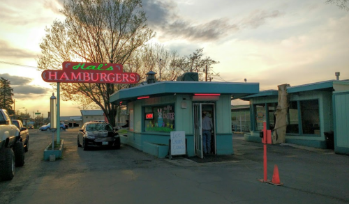 A retro diner named Hal's Hamburgers with a neon sign, featuring a car parked outside and a person entering.