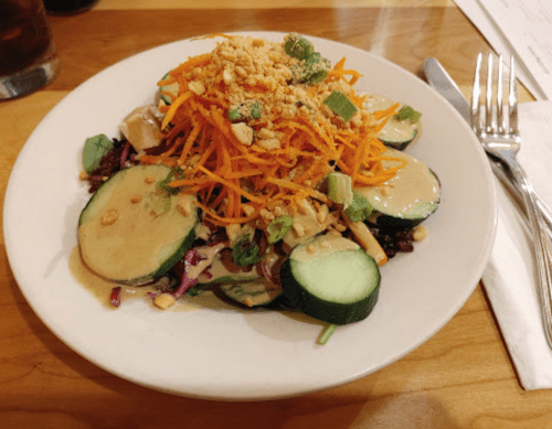 A colorful salad with cucumbers, carrots, and mixed greens topped with peanuts and a light dressing on a white plate.