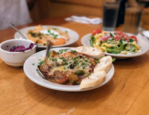 Three plates of food on a wooden table: a savory dish with vegetables, a salad, and a side of pickled onions.