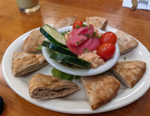 A plate of pita bread triangles with hummus, cucumber slices, cherry tomatoes, and pickled vegetables.