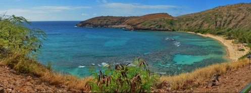 A panoramic view of a serene beach with clear blue waters, coral reefs, and lush green hills under a bright sky.