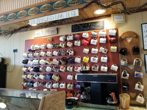 A wall display of colorful coffee mugs above a coffee machine in a cozy café setting.