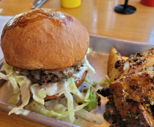 A juicy burger with lettuce and sauce on a bun, served with seasoned potato wedges on a metal tray.