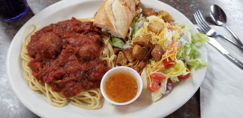 A plate of spaghetti with meatballs in marinara sauce, a side salad, croutons, and a piece of bread.