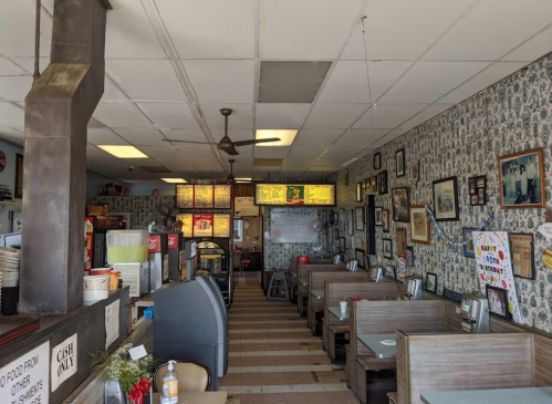 A cozy diner interior with patterned wallpaper, booths, and a menu board, featuring vintage decor and a warm atmosphere.