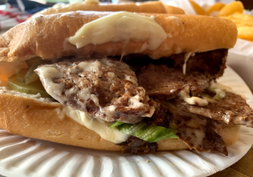 A close-up of a sandwich with two beef patties, lettuce, pickles, and mayonnaise on a toasted bun.