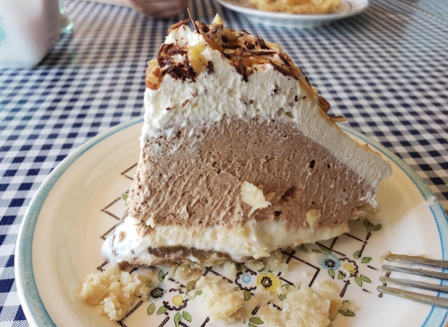 A slice of chocolate cream pie topped with whipped cream and chocolate shavings on a floral-patterned plate.