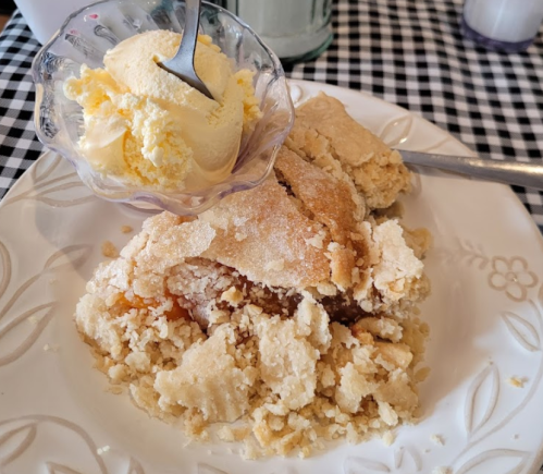 A plate with a serving of crumbly dessert and a scoop of vanilla ice cream in a glass dish.