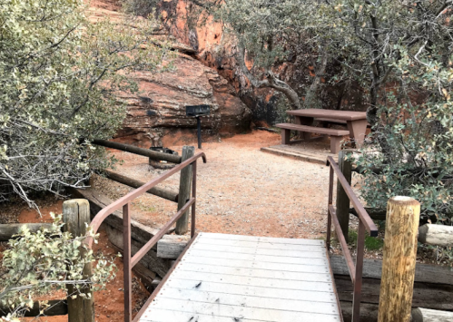 A wooden bridge leads to a picnic area surrounded by rocky terrain and greenery.