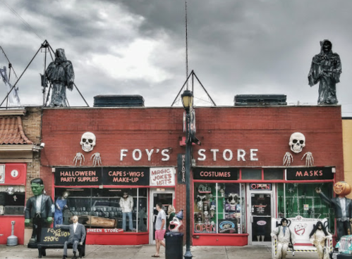 A spooky storefront with Halloween decorations, masks, and figures, including skeletons and a Frankenstein-like character.