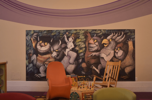 A colorful mural featuring whimsical creatures and a child, set in a playful room with toys and seating.