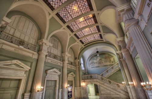 Elegant interior of a grand hall featuring arched ceilings, ornate details, and a sweeping staircase.