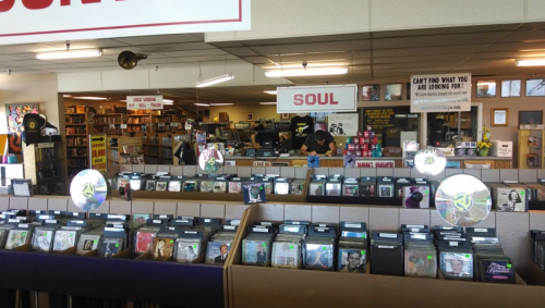 A record store interior with shelves of CDs, a "SOUL" sign, and a staff member assisting a customer.