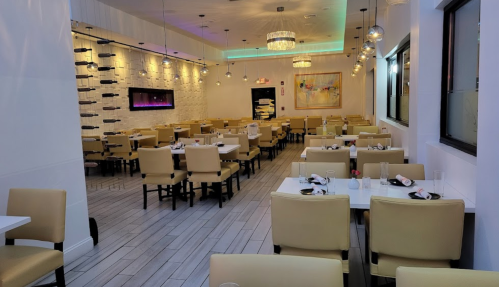 A spacious, modern restaurant interior with white walls, yellow chairs, and tables set for dining.