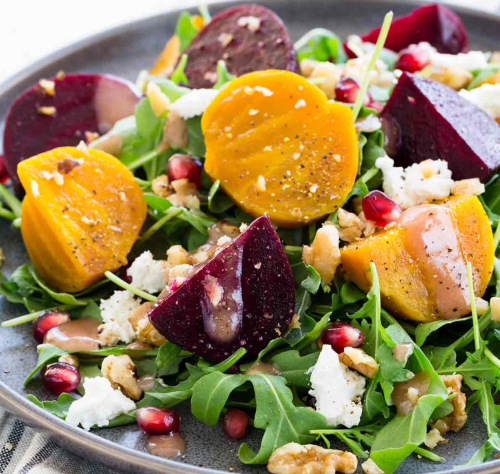 A vibrant salad with mixed greens, roasted beets, pomegranate seeds, walnuts, and crumbled feta cheese.