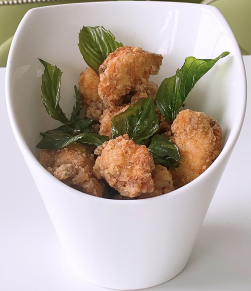 A white bowl filled with crispy fried chicken pieces garnished with fresh basil leaves.