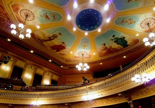 Interior of a grand theater featuring ornate ceiling artwork and elegant chandeliers.
