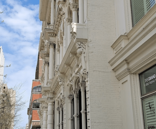 Close-up of ornate architectural details on a white building, with blue sky and clouds in the background.