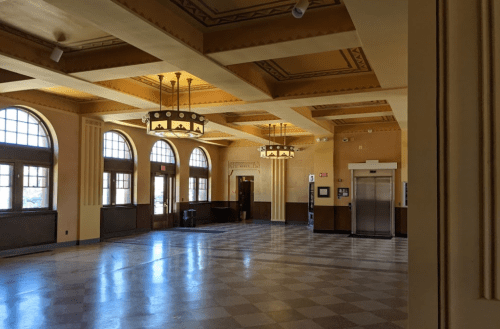 A spacious, well-lit lobby with large windows, decorative chandeliers, and a checkered floor.
