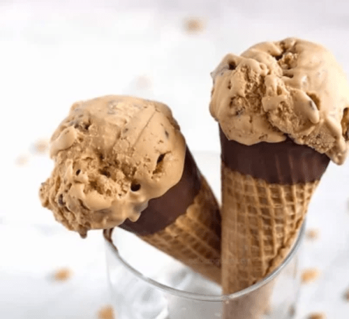 Two ice cream cones with coffee-flavored scoops, topped with chocolate, placed in a glass.