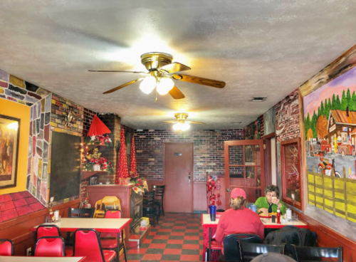 Cozy diner interior with red and black checkered floor, ceiling fan, and colorful wall murals. Two patrons seated at a table.
