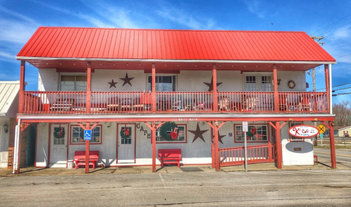 A two-story building with a red metal roof, featuring a porch with stars and holiday decorations.