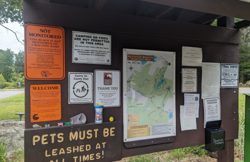 Information board at a park with rules, maps, and notices about camping, pets, and safety guidelines.