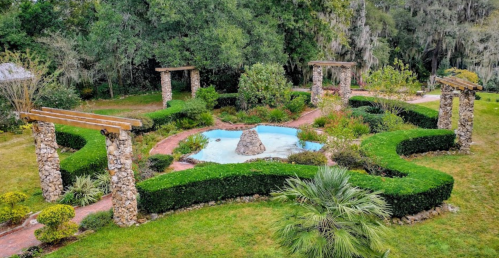 Aerial view of a landscaped garden featuring a circular pond, stone pathways, and neatly trimmed hedges.