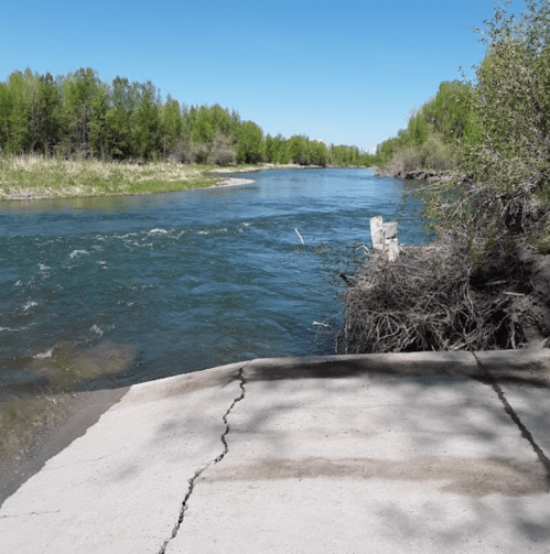 A serene river flows through a lush green landscape under a clear blue sky.