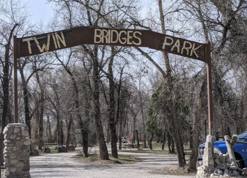 Sign for Twin Bridges Park, surrounded by trees and a gravel path leading into the park.