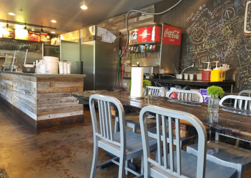 A rustic restaurant interior with wooden tables, chairs, and a chalkboard wall, featuring a counter and drink station.