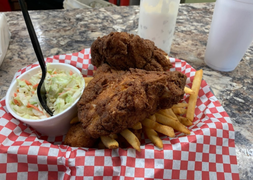 A plate of fried chicken with coleslaw and French fries, served on red-checkered paper.