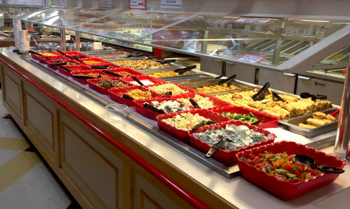 A buffet table with various dishes in red trays, including salads, appetizers, and entrees, under bright lighting.