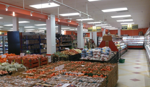 A grocery store aisle filled with fresh produce, including fruits and vegetables, and shelves stocked with various goods.