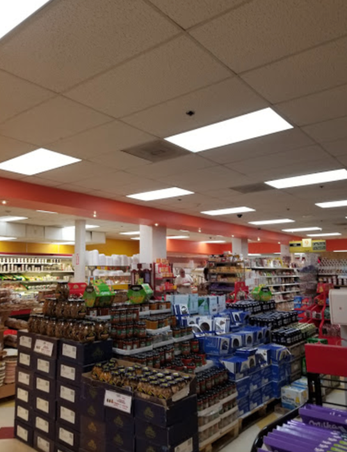 A grocery store aisle filled with shelves of products, including jars and boxes, under bright ceiling lights.