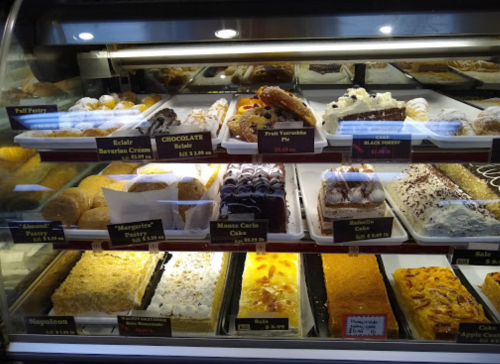 Display case filled with various pastries and desserts, including éclairs, cakes, and tarts, all labeled with prices.