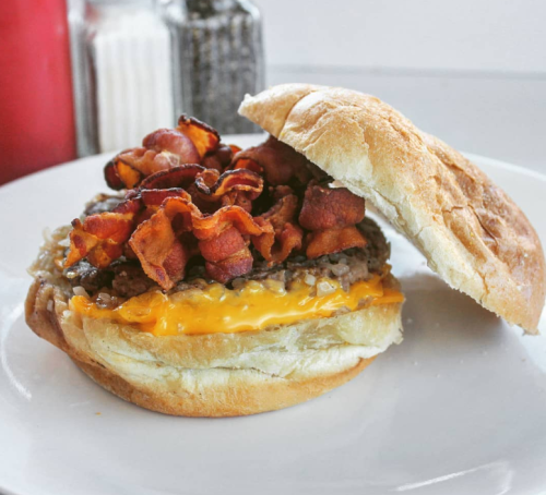 A close-up of a burger with melted cheese, crispy bacon, and sautéed onions on a soft bun, served on a white plate.