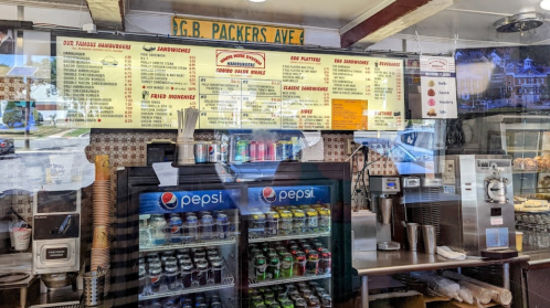 Menu board and drink display at a diner, featuring sandwiches, burgers, and beverages. Brightly lit and inviting atmosphere.