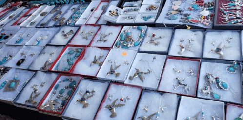 A display of various silver and gemstone jewelry pieces arranged in boxes at a market.