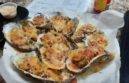 A platter of baked oysters topped with melted cheese and breadcrumbs, served on a white paper liner.