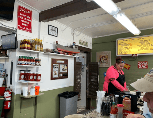 A woman in an apron stands behind a counter with condiments and a sign that says no outside food or drink allowed.