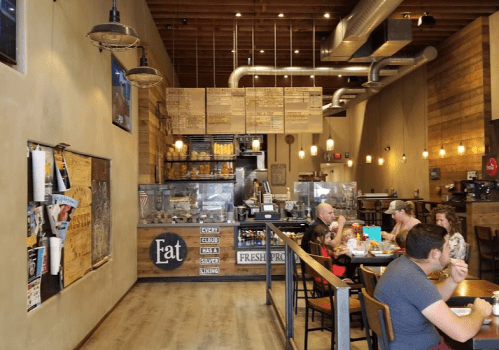 Interior of a cozy café with wooden decor, a menu board, and customers enjoying meals at tables.
