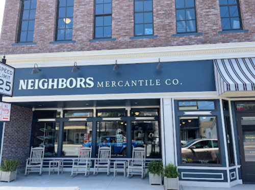 Exterior of Neighbors Mercantile Co. featuring a brick building, large windows, and outdoor seating.